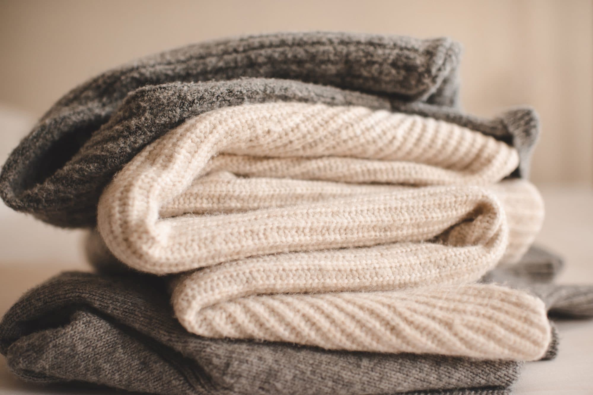 Folded knitwear in cream and grey wool, stacked on a shelf